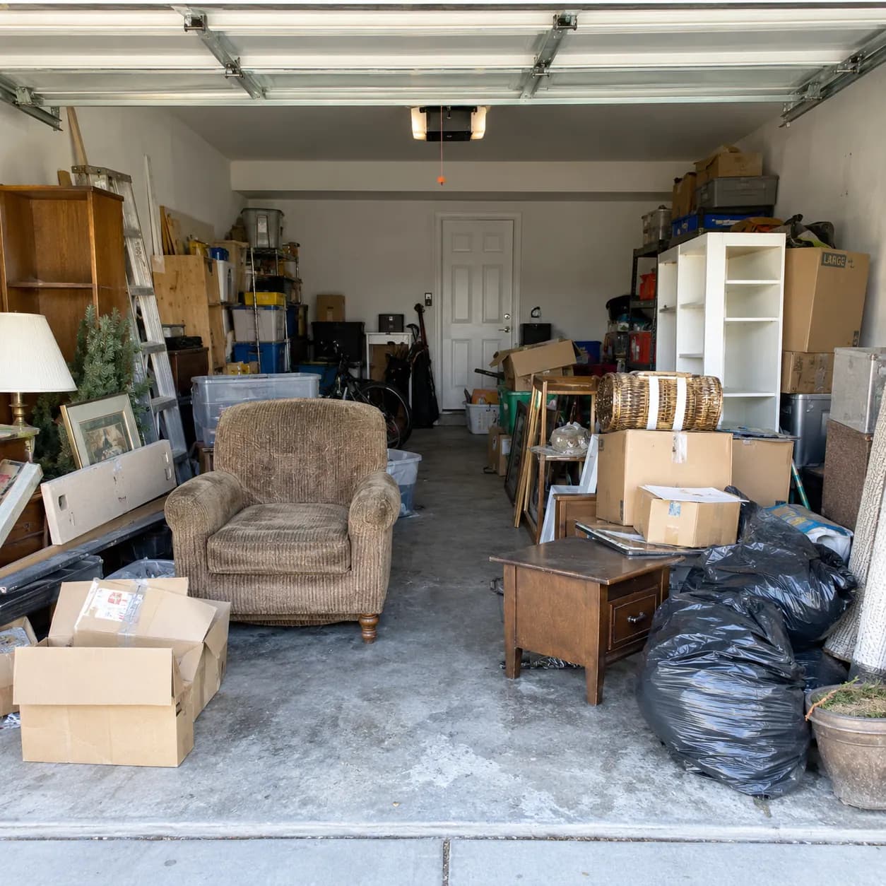 A two-car Fort Worth garage packed with boxes, an armchair, shelving and bagged clutter before a cleanout